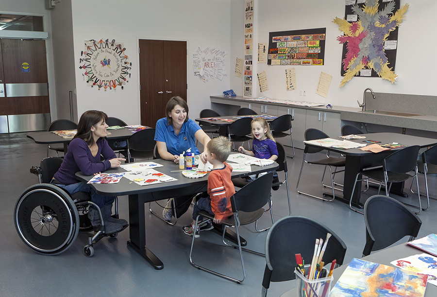 A person in a wheelchair, others, and children painting art around a table.