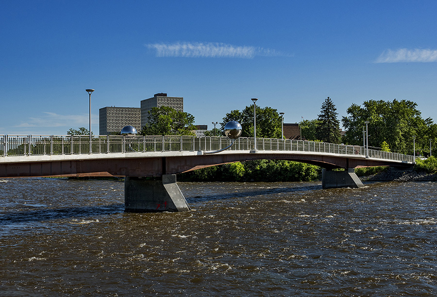 Pedestrian bridge with two polished balls over turbulent river.