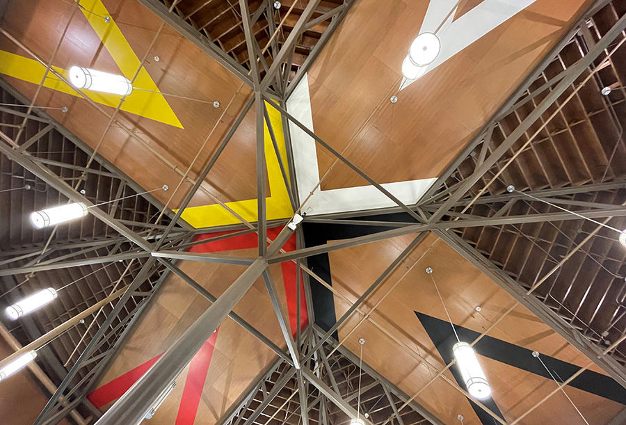 Looking up at a steel and wood structure with red, yellow, white, and black painted patterns indicated cardinal directions.