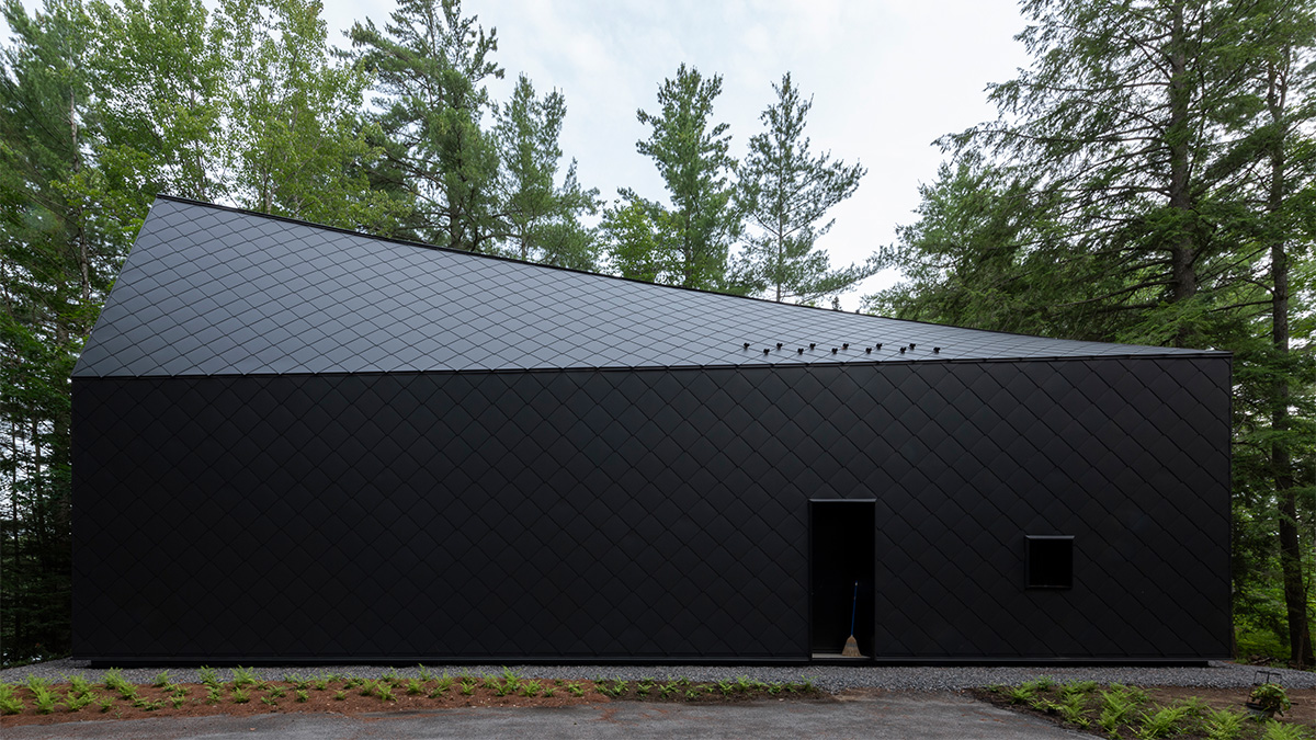 A black building with diamond cladding and a sloped roof, surrounded by forest