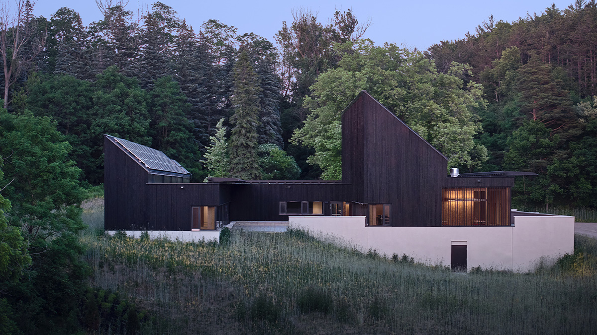 A geometric building with dark wood siding and angled rooflines, set on a grassy hillside