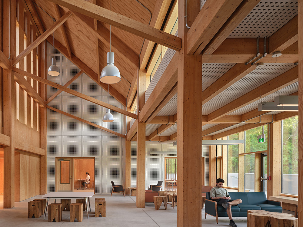 A timber‑framed interior with high ceilings, large windows, and people sitting in a seating area