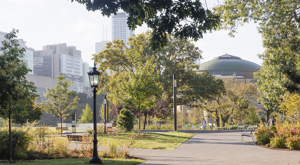 A landscaped park walkway leads toward a domed building with city towers rising behind