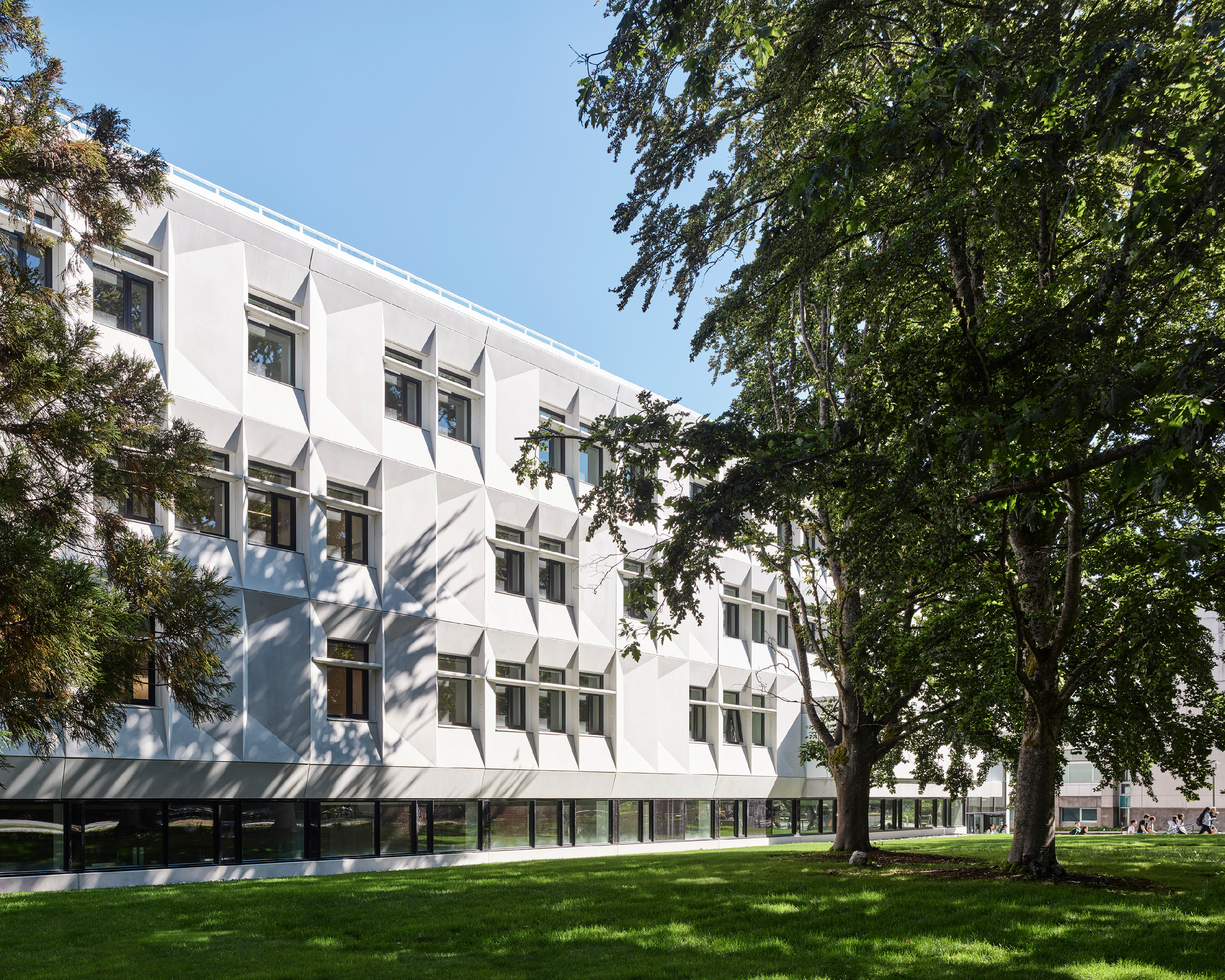 A white institutional building with geometric windows surrounded by a lawn and trees
