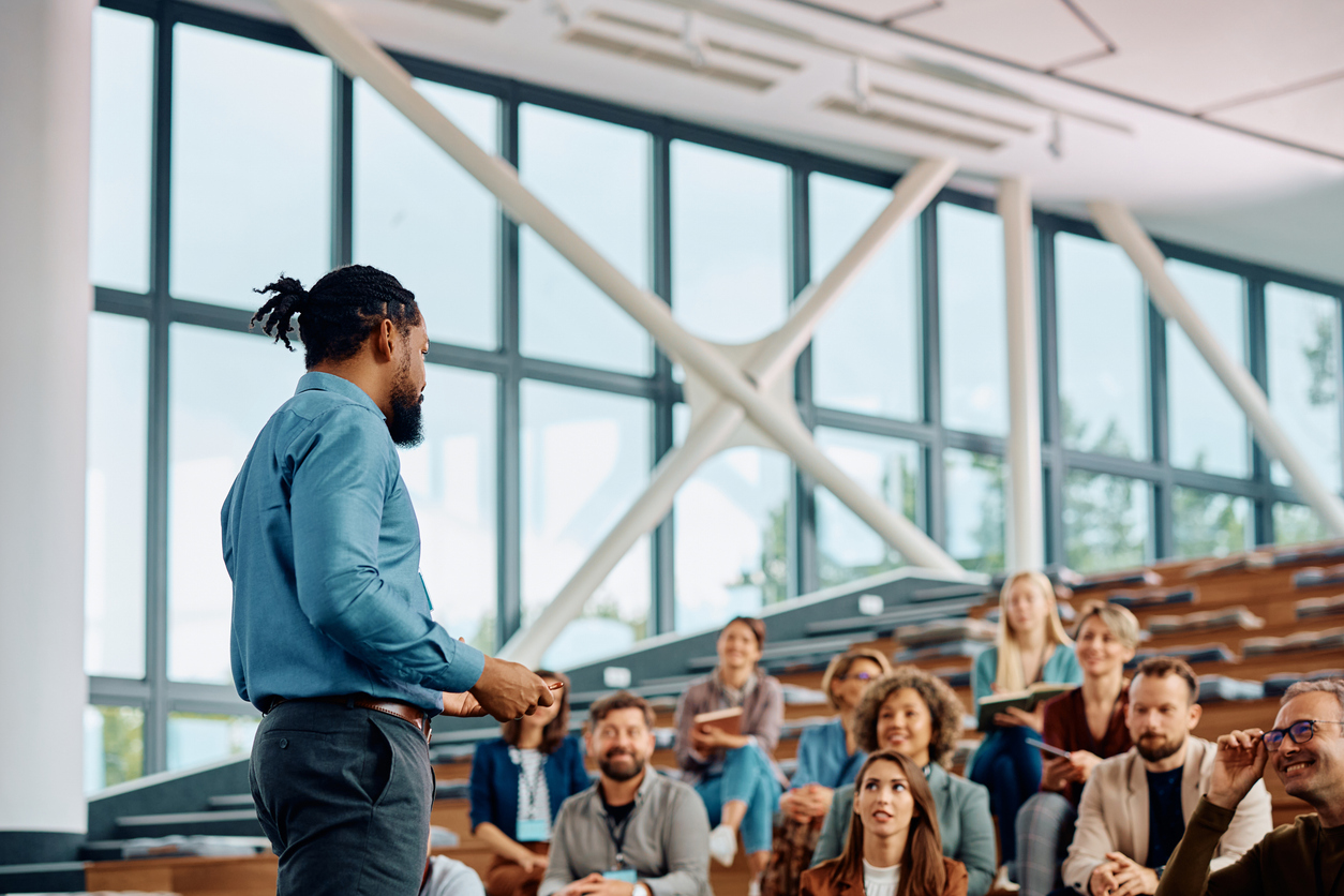 Image a speaker standing leading  a session with guests looking on intently