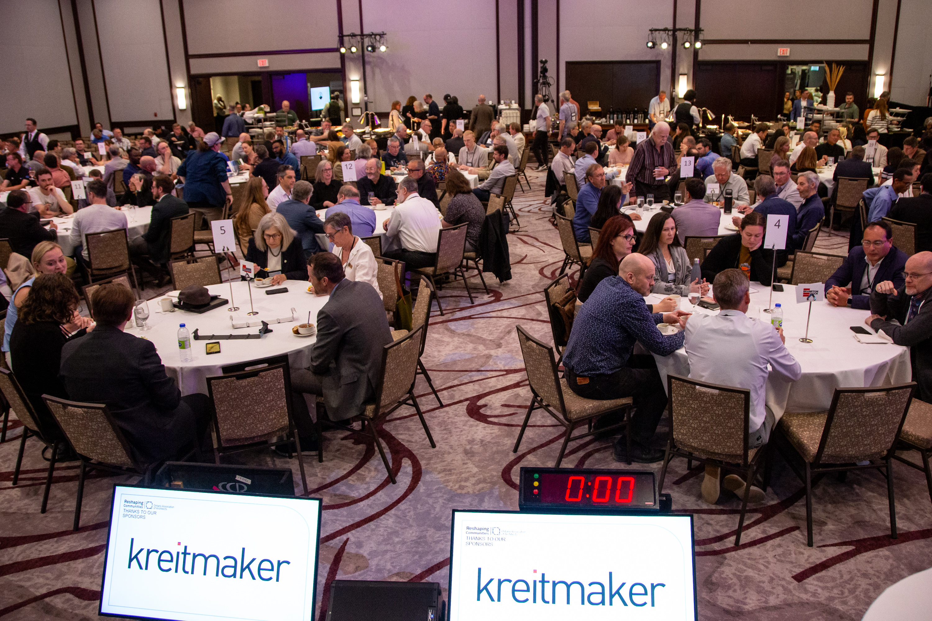 Crowd shot of the Ask the Experts luncheon, In the bottom foreground, there are screens featuring the Kreitmaker logo