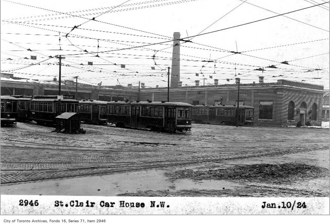  In black and white, three streetcars are stationed in a muddy yard in front of the five car-barns.