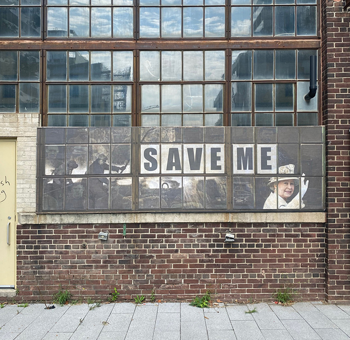  A poster applied to the industrial windows of one of the buildings of the foundry complex. The poster has bold letters with the words“Save Me” and historical images of foundry workers and Queen Elizabeth II..
