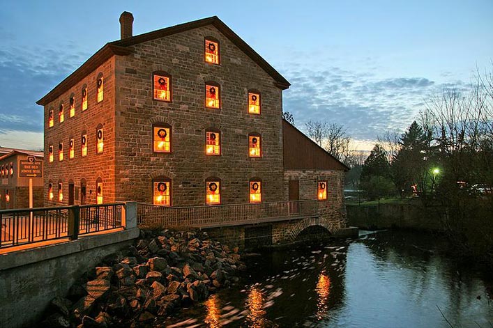 Light from the Old Stone Mill's symmetrical windows glows warmly and is reflected in the water around the building.