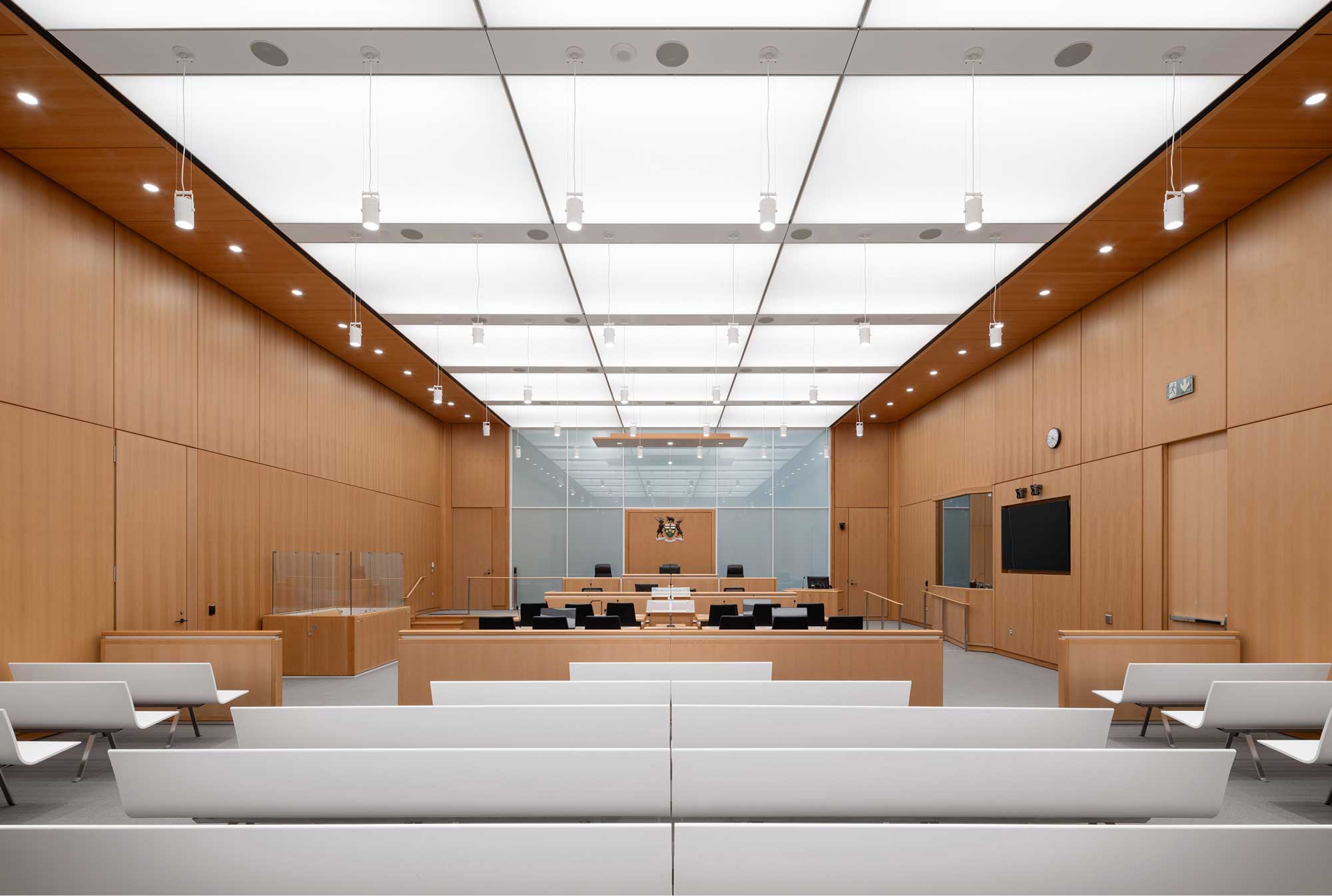 Ceremonial Courtroom with white solid surface custom public seating, beech paneling and millwork, luminous ceiling and translucent Dias wall allowing exterior daylight penetration