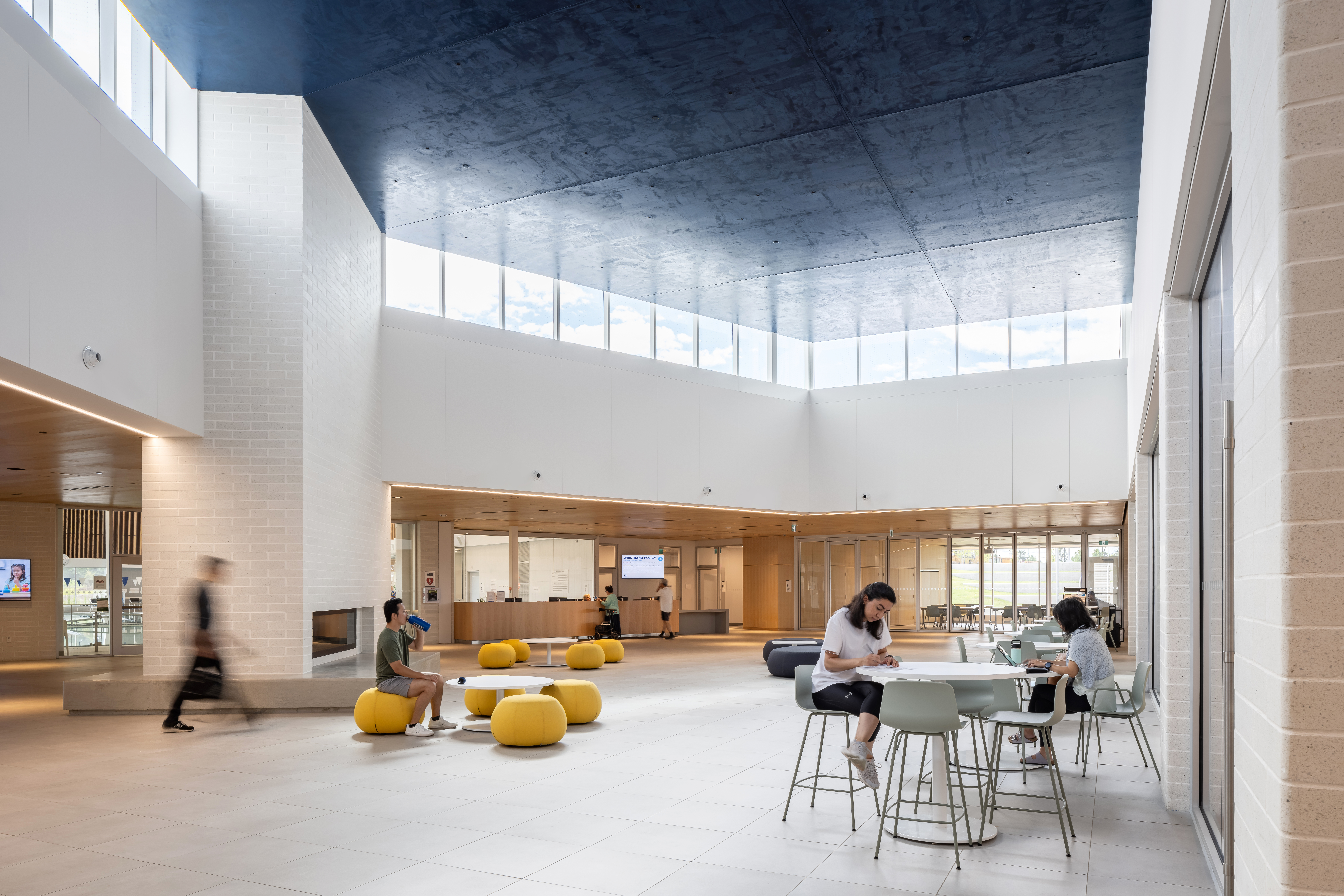 Interior view of the "Heart", a modern communal space with a dark-blue ceiling inspired by the night sky, tall windows, light flooring, and seating areas. People are  working and socializing.