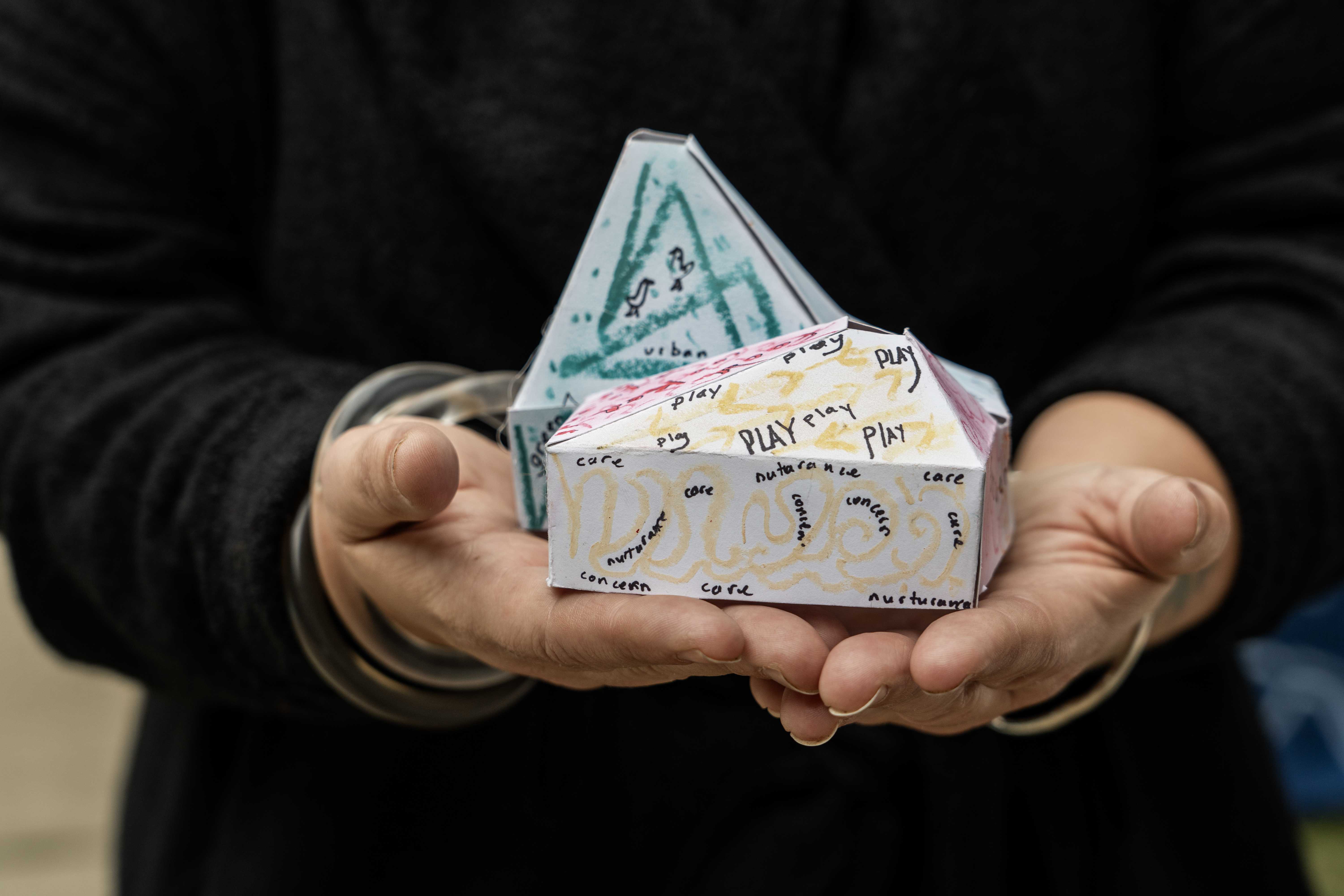 A handmade paper model of "The Belle," created by the community, held in cupped hands.