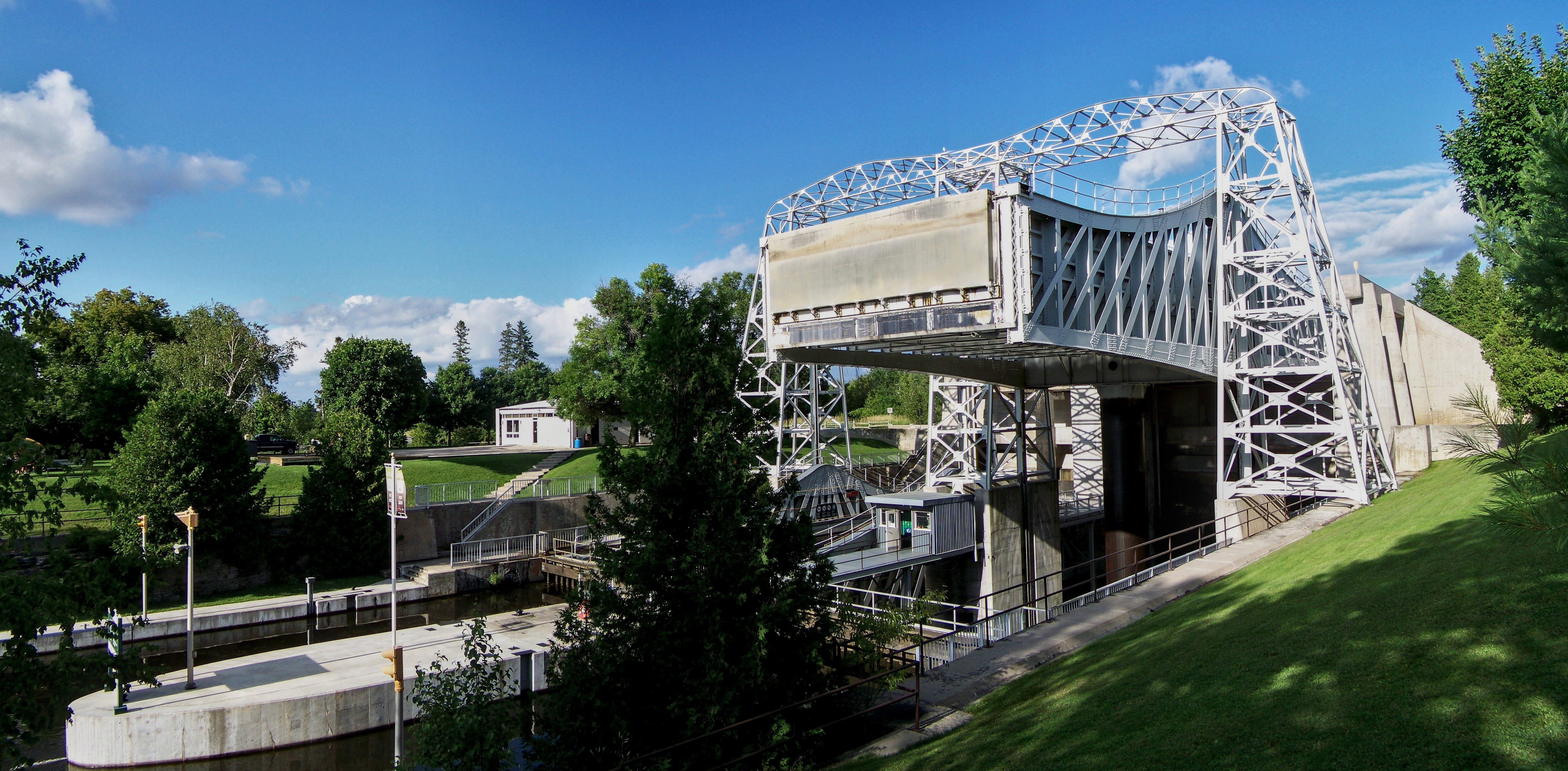 Exterior view of large, white-painted steel structure straddling a canal with one boat lift chamber in up position. 
