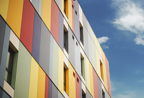 Close-up view of a building facade featuring vertical panels in a variety of colors, including red, yellow, orange, blue, and gray. The facade has rectangular windows spaced throughout.