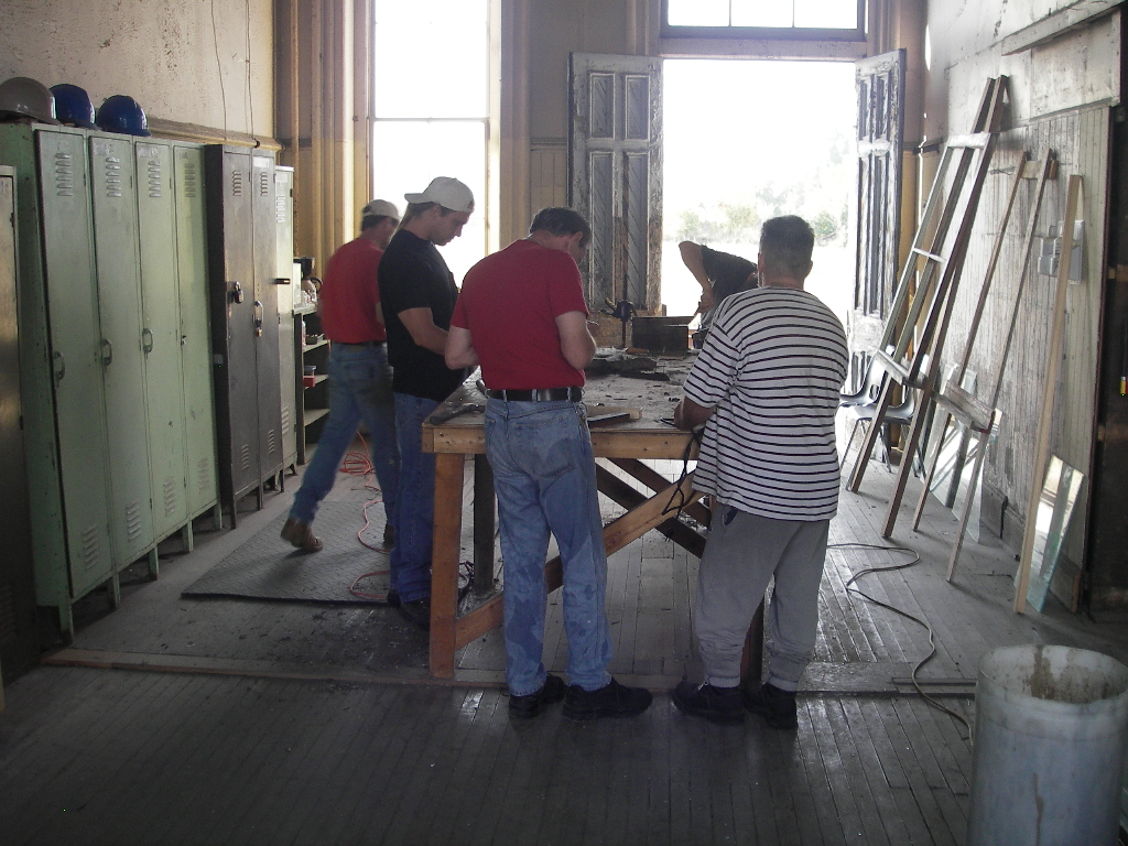 A group of volunteers gather around a workbench in a workshop, showcasing the collaborative effort behind the CASO station's restoration.