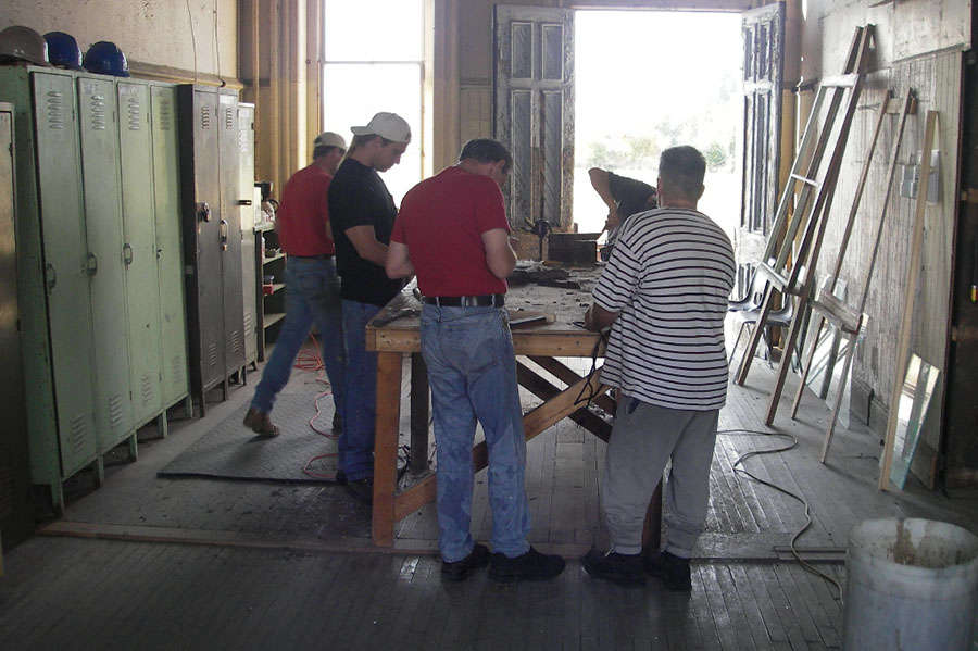 A group of volunteers gather around a workbench in a workshop, showcasing the collaborative effort behind the CASO station's restoration.