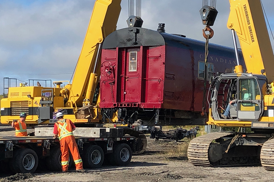 Workers using cranes to move vintage railcars from the yard to their new location.