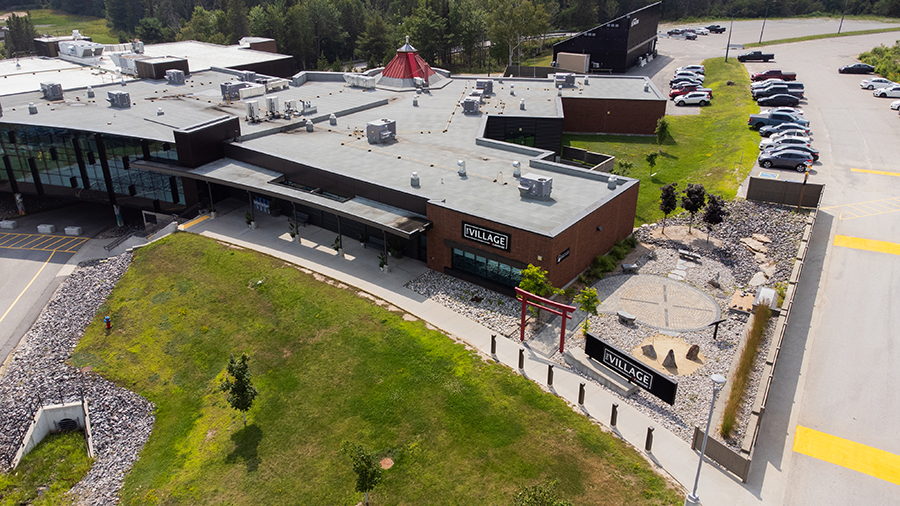 Aerial view of The Village, showcasing modern buildings with flat roofs, green spaces, parking lots, and a landscaped area featuring a red torii gate and rock garden.
