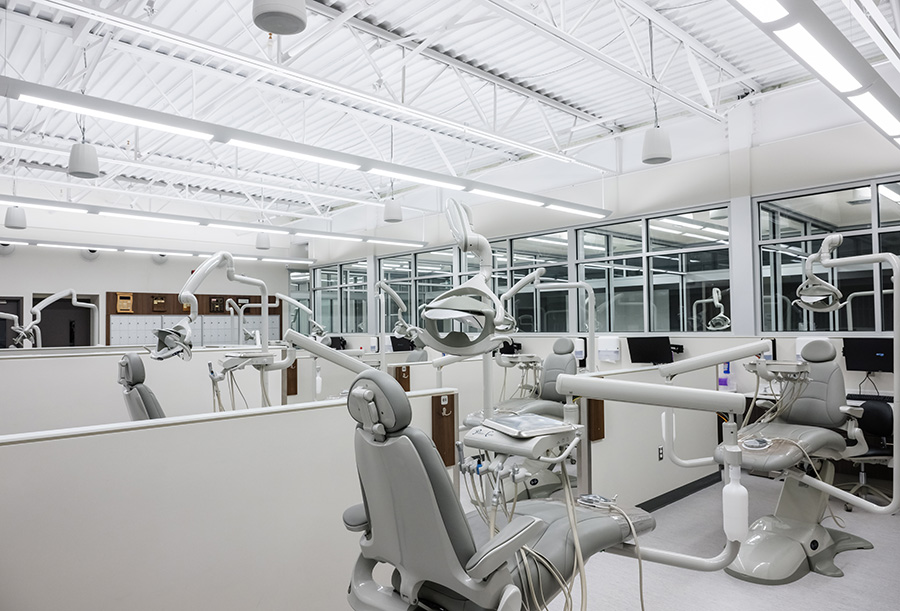 Interior view of a bright, modern dental lab with multiple  gray dental stations, each equipped with chairs, lights, and dental tools.