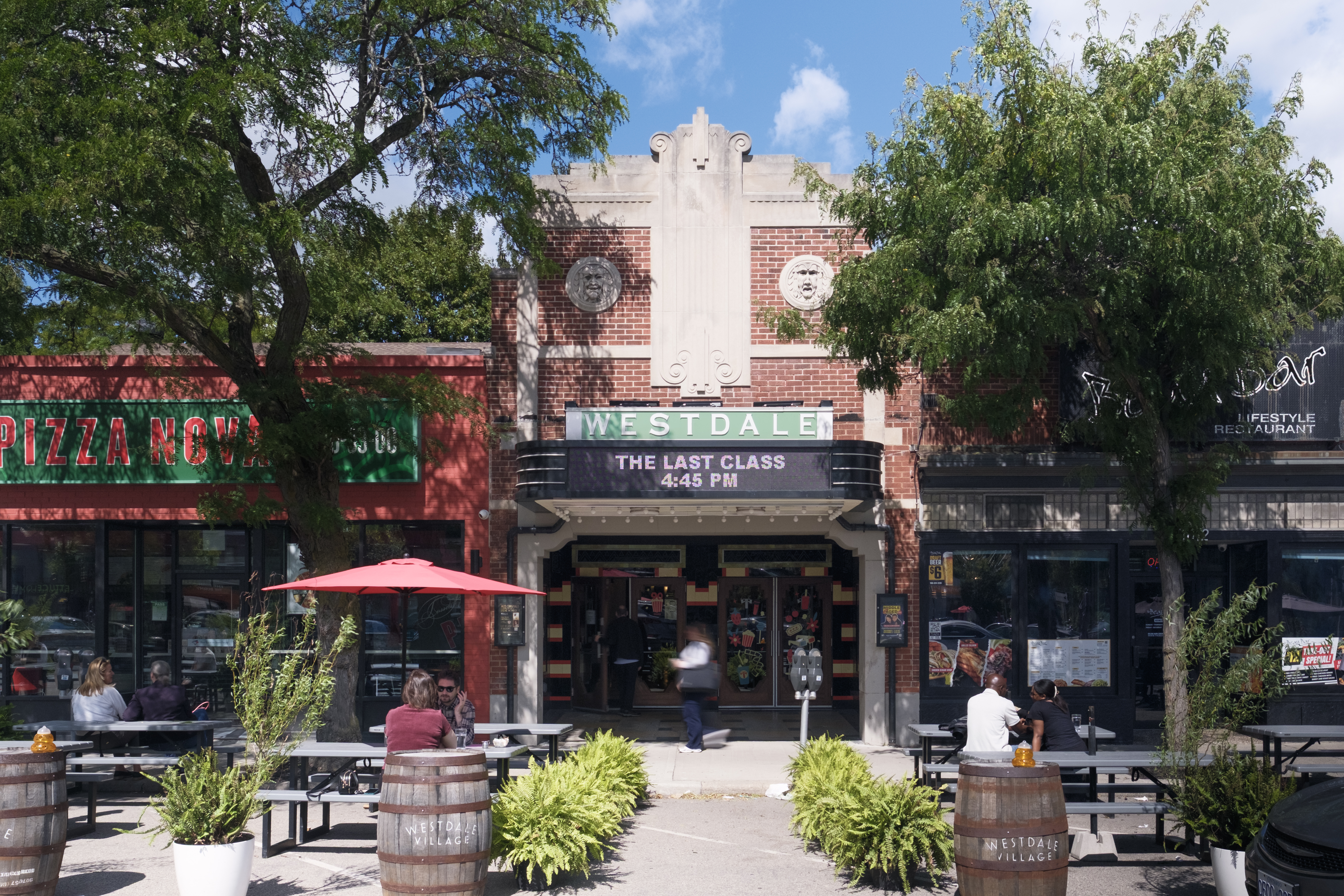 Exterior view of the Westdale Theatre, displaying its new marquee and its integration with neighbouring storefronts, including a pizza place and a restaurant with outdoor seating.