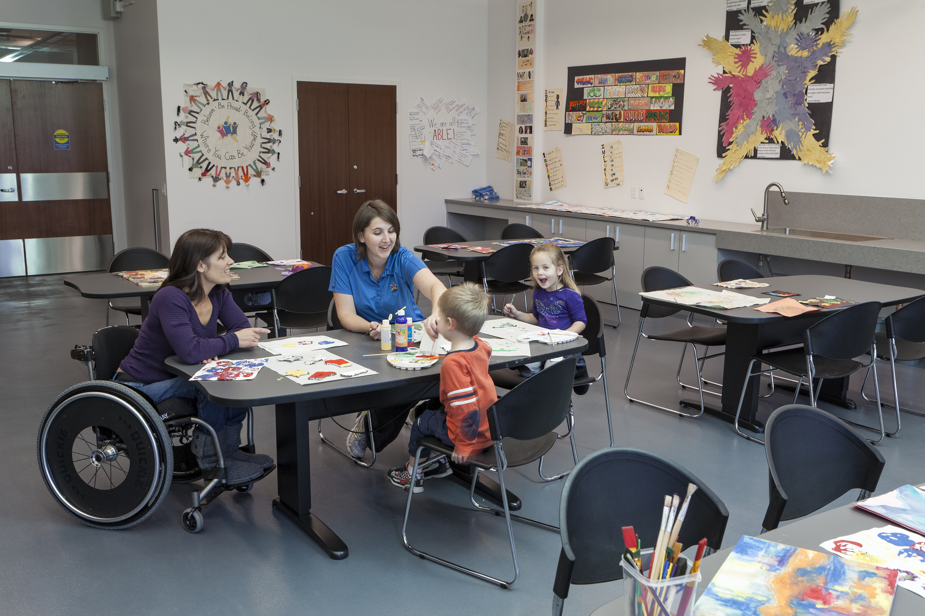 A person in a wheelchair, others, and children painting art around a table.